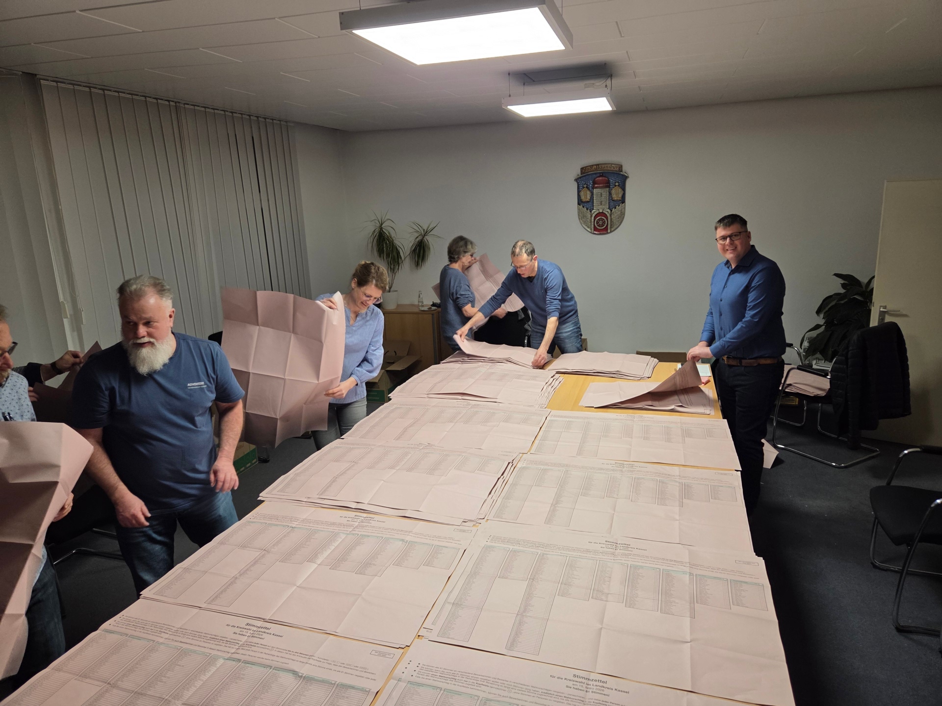 Wahlhelfer sortieren Stimmzettel auf einem großen Tisch im Sitzungszimmer