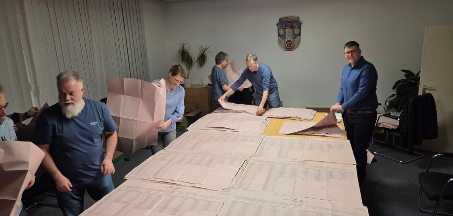 Wahlhelfer sortieren Stimmzettel auf einem großen Tisch im Sitzungszimmer