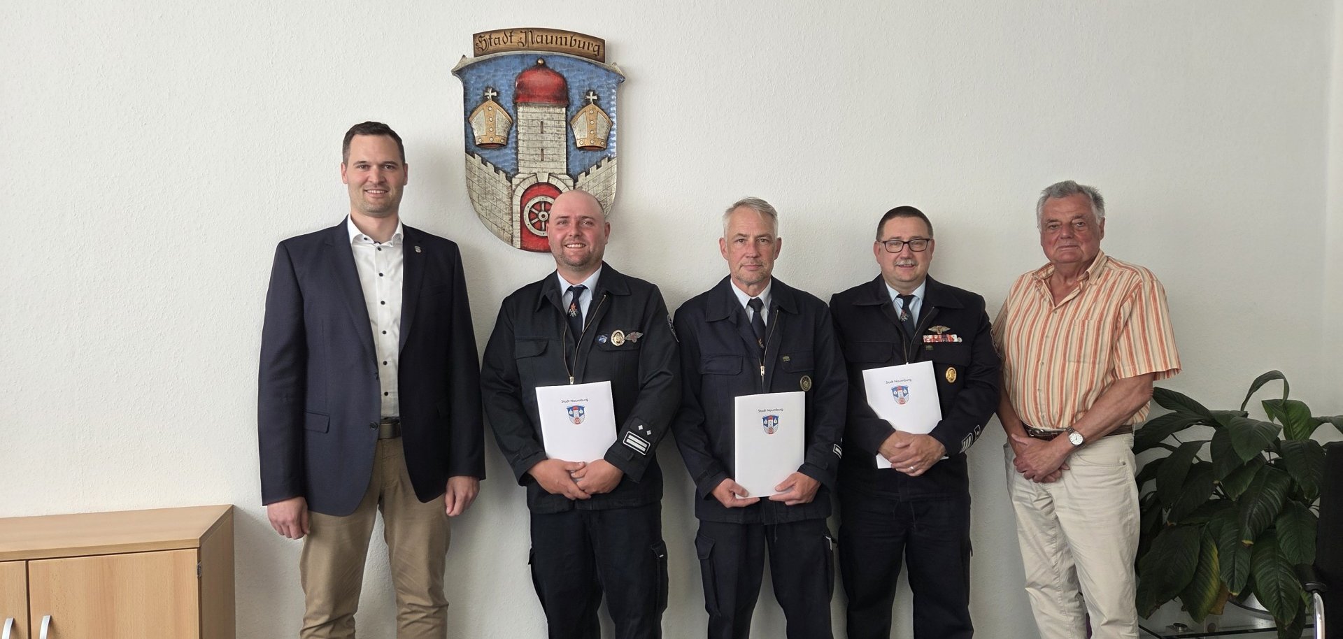 Personen stehen in einem Raum vor einem Stadtwappen