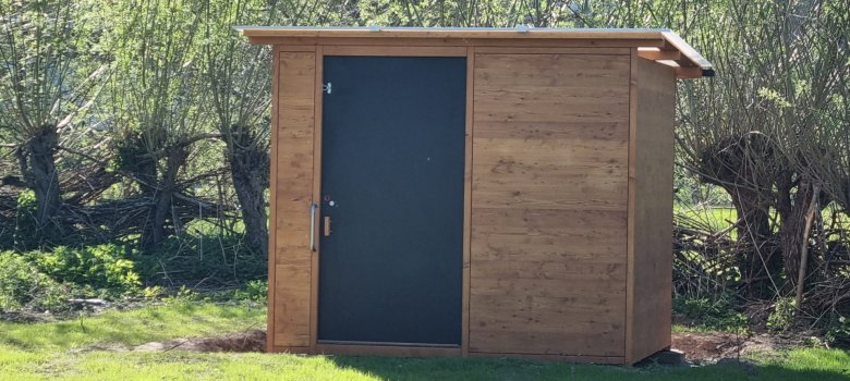 Komposttoilette vor Bäumen auf einer grünen Wiese