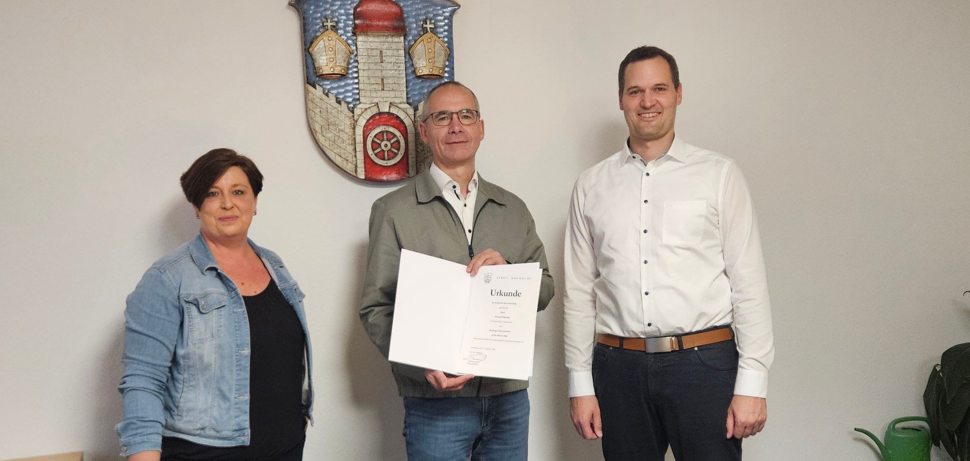 Personen stehen in einem Raum vor einer Wand mit Stadtsiegel