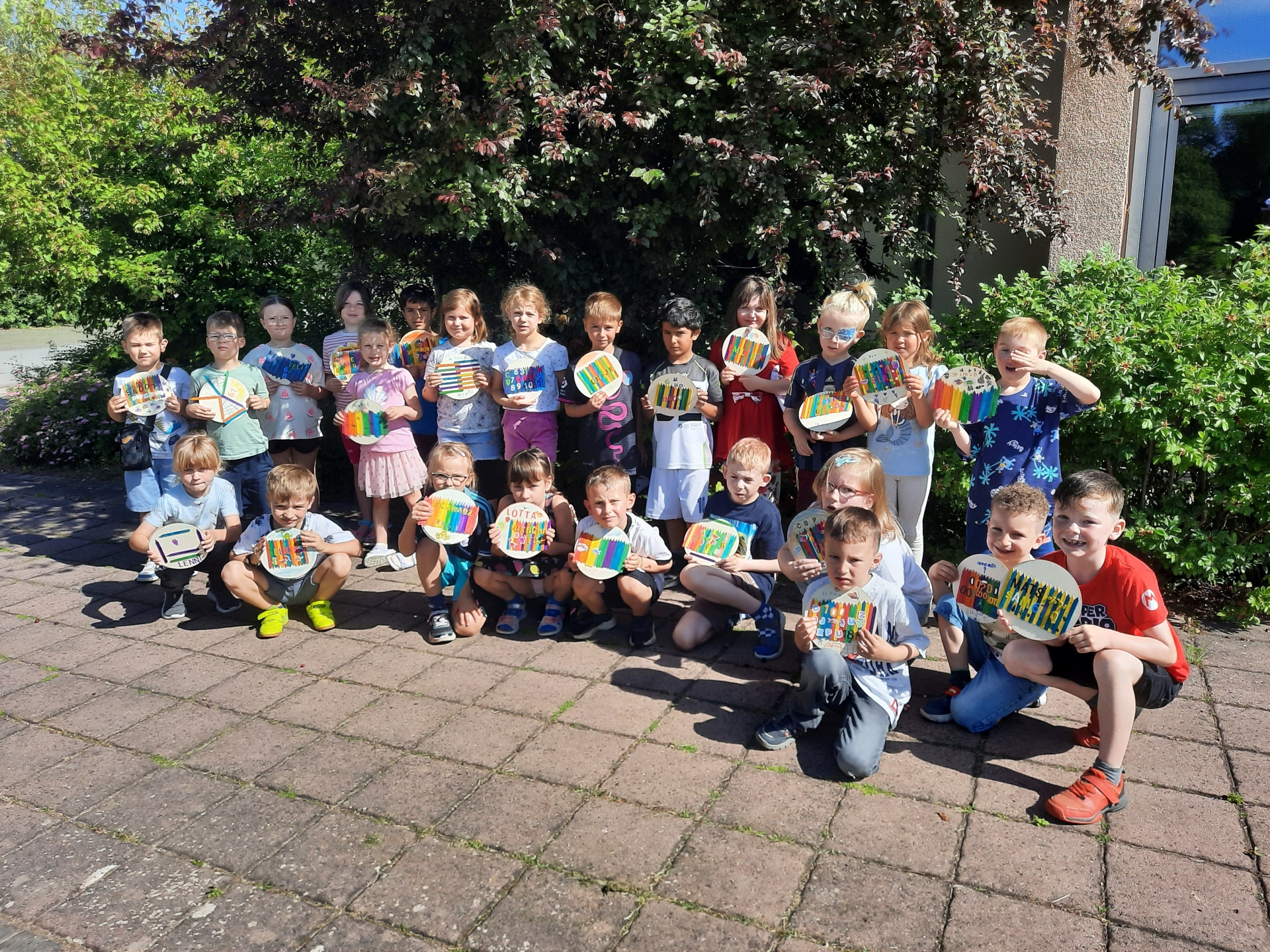Vorschulkinder vor einem Strauch mit gebastelten Namensschildern in der Hand