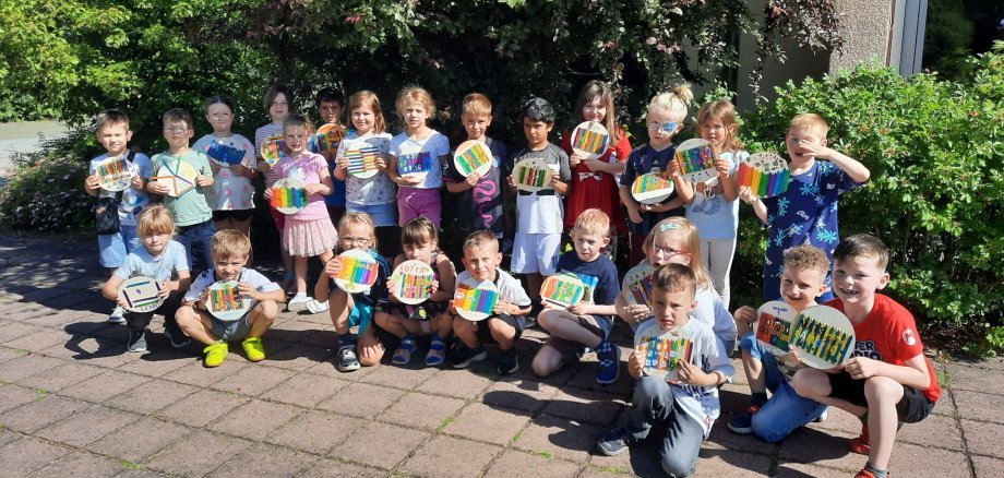 Vorschulkinder vor einem Strauch mit gebastelten Namensschildern in der Hand