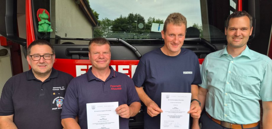 Vier Personen stehen vor einem Feuerwehrauto