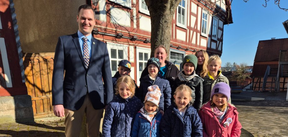 Vorschulkinder stehen mit Bürgermeister auf dem Marktplatz vor einem Baum und Haus